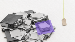 Una gran pila desordenada de carpetas y papeles en blanco y negro ocupa la izquierda; un pequeño montón queda ordenado bajo papel morado. A la derecha cuelga una etiqueta de precio vacía y diminuta, mientras el trabajo de organizar el proceso conserva el peso visual.